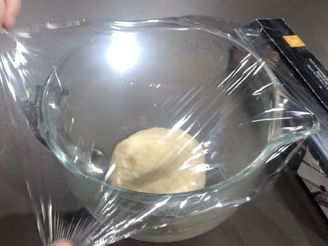 La boule de pâte est déposée au fond de la cuve du batteur qui est recouverte d'une feuille de papier film