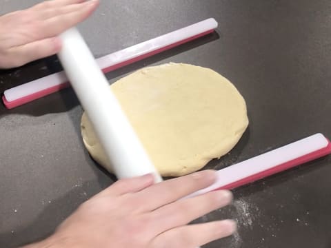 La pâte à beignets est étalée au rouleau à pâtisserie sur le plan de travail, entre deux réglettes à niveler