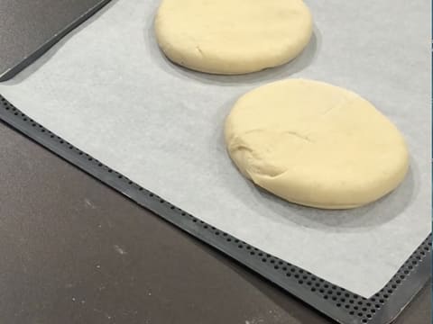 Obtention de deux disques de pâte à beignets posés sur une plaque de cuisson perforée recouverte d'une feuille de papier sulfurisé