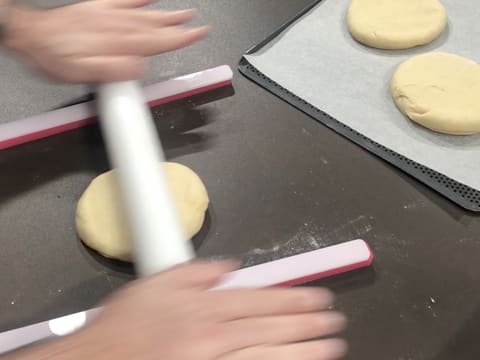 La pâte à beignets est étalée au rouleau à pâtisserie sur le plan de travail, entre deux réglettes à niveler