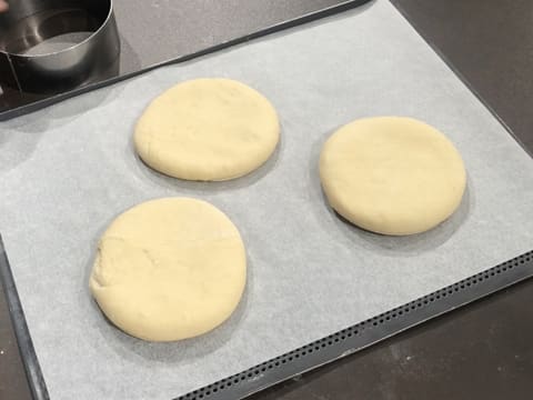 Obtention de trois disques de pâte à beignets posés sur une plaque de cuisson perforée recouverte d'une feuille de papier sulfurisé