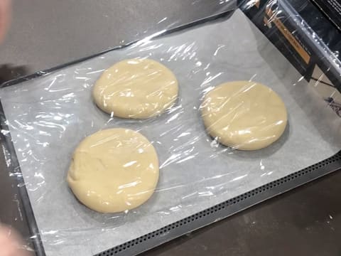 Les trois disques de pâte à beignets posés sur une plaque de cuisson perforée recouverte d'une feuille de papier sulfurisé, sont filmés au contact avec une feuille de papier film