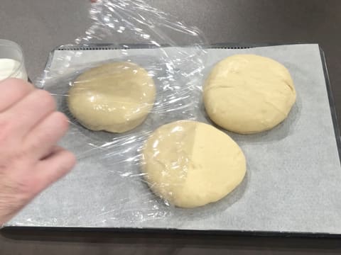 La feuille de papier film est retirée des disques de pâte à beignets qui ont poussé sur la plaque de cuisson perforée recouverte d'une feuille de papier sulfurisé