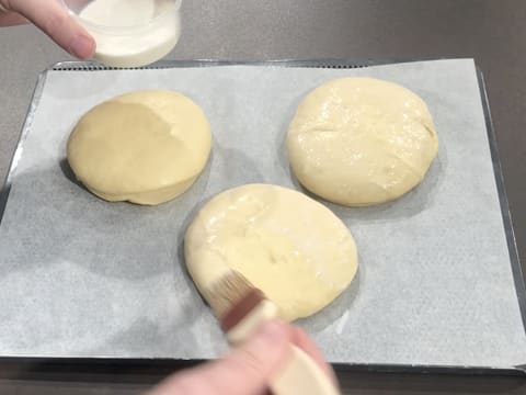Les trois beignets crus sont badigeonnés de lait à l'aide d'un pinceau pâtissier