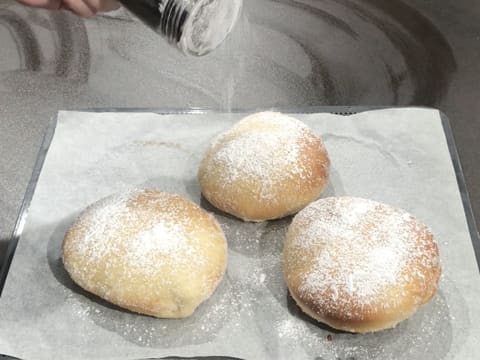 Les trois beignets sont placés sur des feuilles de papier absorbant et sont saupoudrés de sucre glace