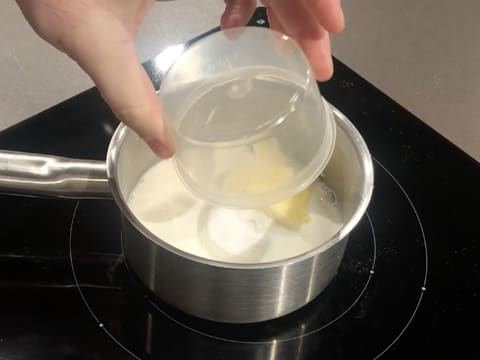 Ajout du beurre dans le lait et le sucre en poudre qui se trouvent dans la casserole posée sur la plaque de cuisson
