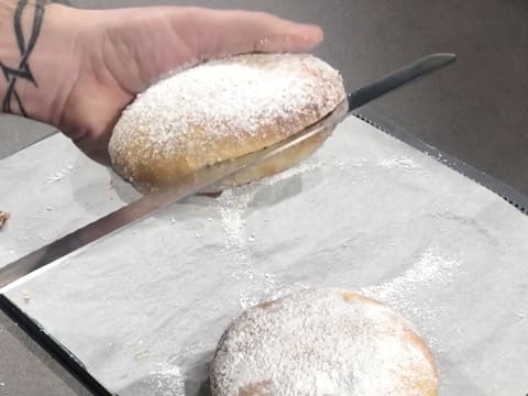 Un beignet décoré de sucre glace est coupé en deux dans l'épaisseur à l'aide d'un couteau scie à génoise