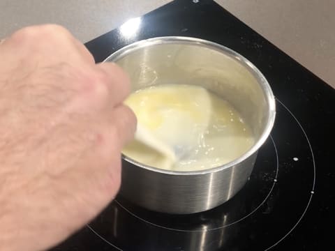 Fonte du beurre dans la préparation lactée qui est mélangée à l'aide d'une spatule, dans la casserole qui est sur la plaque de cuisson