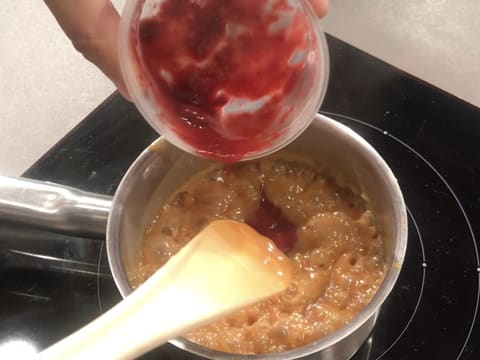 Ajout de la purée de framboise dans la sauce caramel qui se trouve dans la casserole sur la plaque de cuisson