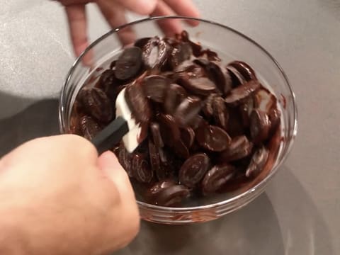 Mélange des fèves de chocolat noir qui commencent à fondre dans le saladier en verre, à l'aide d'une spatule maryse