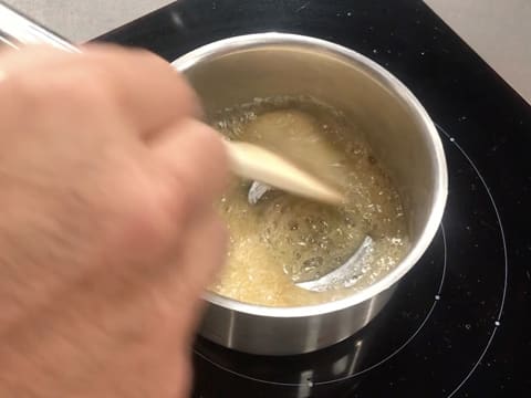 La préparation à base de sirop de glucose et de sucre est en train de bouillir et de devenir caramel dans la casserole tout en étant mélangée avec une spatule