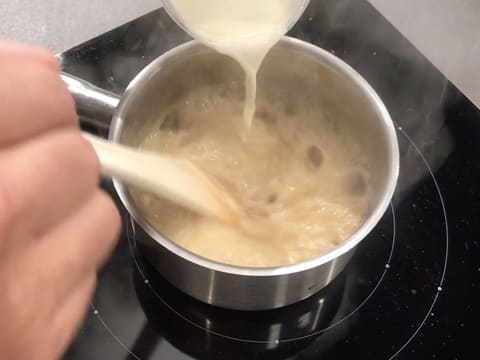 Ajout et incorporation de la crème dans le caramel qui est bouillant dans la casserole, à l'aide de la spatule