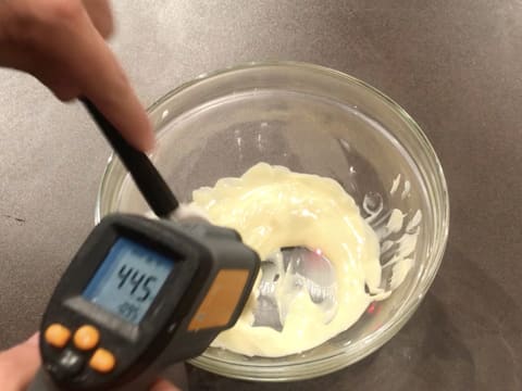 Prise de la température du chocolat blanc fondu dans le saladier en verre à l'aide d'un thermomètre à visée laser qui affiche 44,5°C