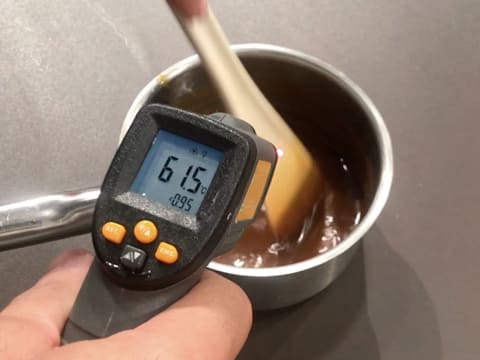 Prise de la température du caramel mangue qui se trouve dans la casserole, avec un thermomètre à visée laser qui affiche 61,5°C