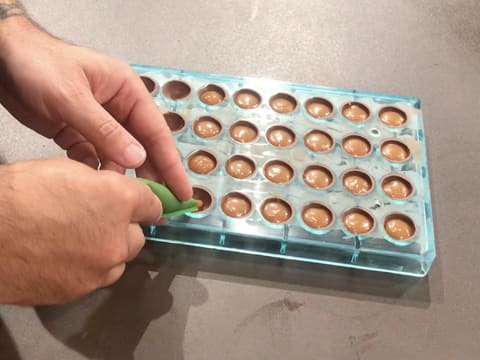 Le caramel mangue est poché à la poche pâtissière dans les empreintes du moule chocolat demi sphère