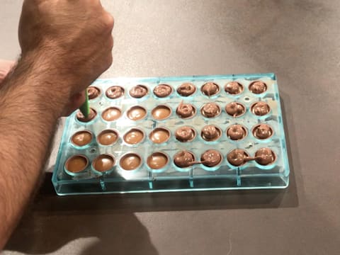 Le chocolat au lait tempéré est poché à la poche à douille dans les empreintes du moule chocolat demi sphère qui est posé sur le plan de travail