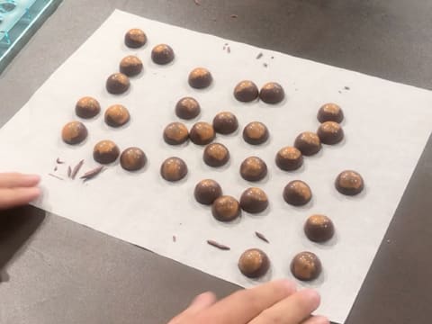Obtention de demi sphères en chocolat qui sont des bonbons caramel mangue, sur le plan de travail recouvert de la feuille de papier sulfurisé