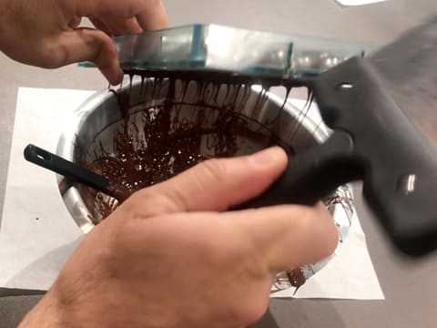 Le moule chocolat demi-sphère retourné au-dessus du cul de poule, est tapoté sur le côté avec une spatule à chocolat, et l'excédent de chocolat s'écoule dans celui-ci