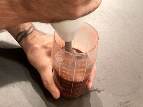 La préparation au chocolat qui est dans un verre doseur est mixée avec un mixeur plongeant