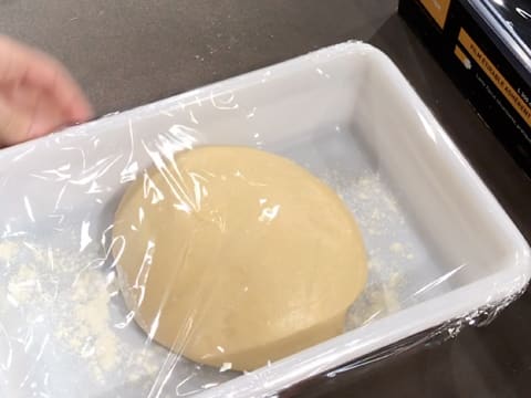 Le bac alimentaire fariné et contenant la boule de pâte à brioche, est filmé avec une feuille de papier film
