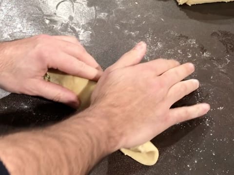 Un pâton de pâte à brioche est aplati et enroulé sur lui-même avec la paume de la main sur le plan de travail légèrement fariné