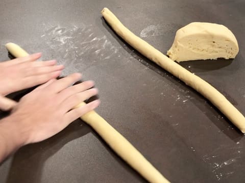 Le deuxième pâton de pâte est roulé avec la paume de la main sur le plan de travail fariné, et forme un long boudin