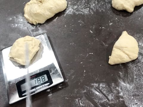 Trois pâtons de pâte à brioche sont sur le plan de travail fariné, et un pâton est placé sur une balance de cuisine électronique qui affiche 188 grammes