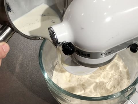 Le lait vanillé contenu dans la casserole est versé dans la cuve du batteur sur les poudres mélangées