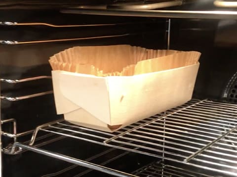 Une brioche contenue dans une barquette de cuisson en bois est placée dans un four