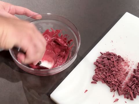 Le chocolat à la framboise dans le saladier est fondu et mélangé à la spatule maryse, et des fèves de chocolat à la framboise sont hachées sur une planche à découper