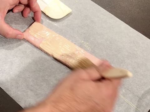 Le rectangle de biscuit macaron est badigeonné de chocolat blanc fondu, à l'aide d'un pinceau pâtissier