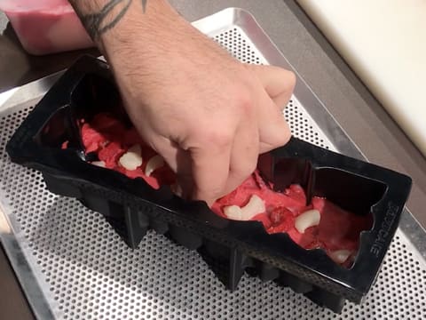 Des morceaux de litchi et de framboise sont piqués dans le sorbet litchi et framboise qui est étalé dans le moule à bûche silicone