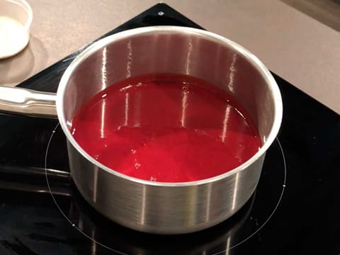 La purée de framboise est placée dans une casserole, sur une plaque de cuisson