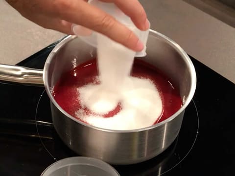 Du sucre en poudre est versé dans la casserole, sur la purée de framboise