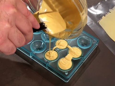 Du chocolat Inspiration passion fondu est versé dans quatre empreintes d'un moule chocolat demi sphère