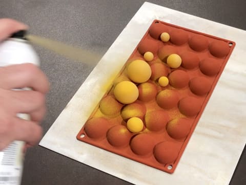 Pulvérisation du colorant en spray effet velours jaune sur un premier côté des décors en chocolat