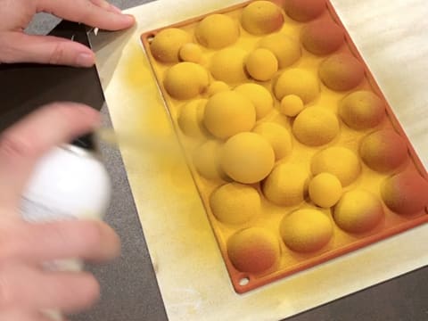 Pulvérisation du colorant en spray effet velours jaune sur l'autre face des décors en chocolat