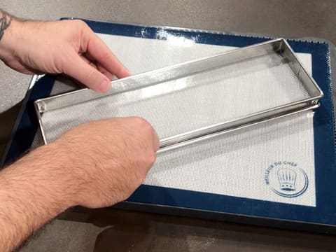 Un cadre à tarte rectangulaire est posé sur un tapis de cuisson silicone, lui-même posé sur une plaque de cuisson perforée