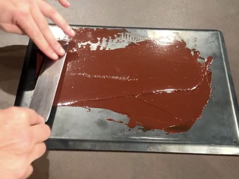 Le chocolat fondu est étalé sur la plaque à pâtisserie avec une spatule coudée