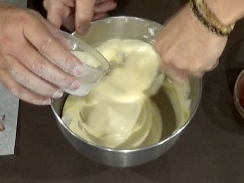 La crème liquide est versée sur les blancs en neige mêlés aux jaunes d'oeufs, dans la cuve du batteur, tout en étant mélangés à la spatule maryse