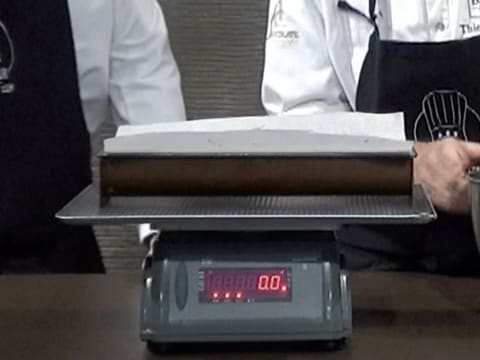 Le moule à bûche chemisé posé sur une plaque à pâtisserie, est placé sur la balance de cuisine électronique