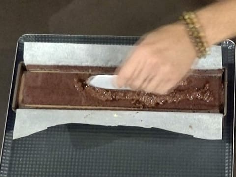 Du croustillant spéculoos est versé sur le biscuit chocolat qui est dans le moule à bûche