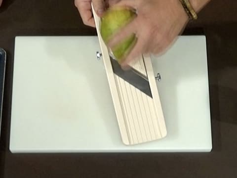 Une poire est émincée avec une mandoline sur une planche à découper