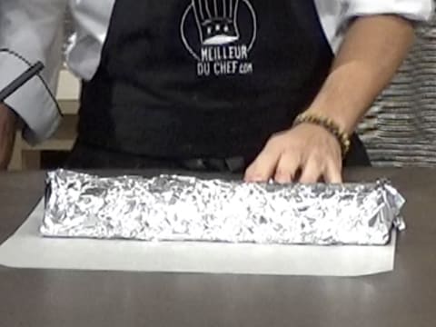 Un moule à bûche est recouvert de papier aluminium et est placé sur une feuille de papier sulfurisé, sur le plan de travail