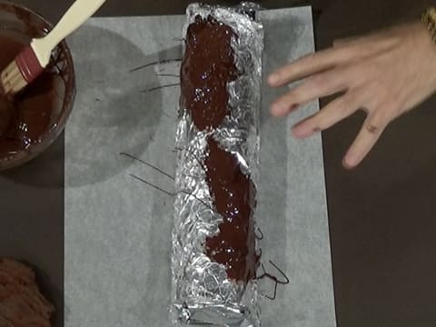 Vue de dessus du chocolat noir fondu étalé sur le papier film qui est sur le papier aluminium sur le moule à bûche