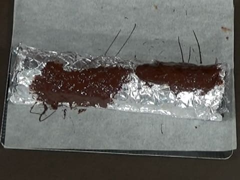Vue de dessus du chocolat noir fondu étalé sur le papier film qui est sur le papier aluminium sur le moule à bûche