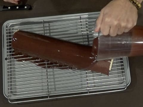 Le glaçage chocolat est versé sur toute la longueur de la bûche qui est posée sur la grille à pâtisserie posée sur la plaque creuse
