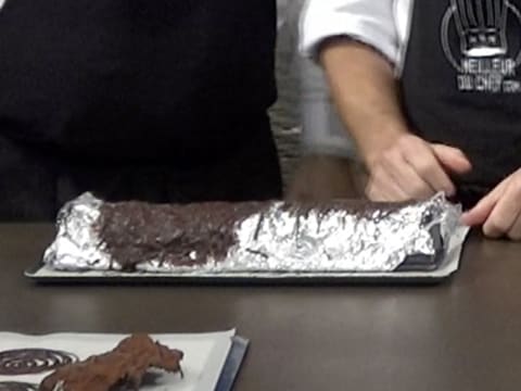 Le moule à bûche recouvert de papier aluminium, de papier film et de chocolat est sur le plan de travail