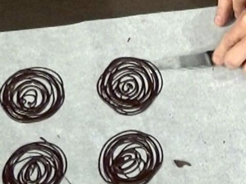 Une spirale en chocolat noir est décollée du papier sulfurisé avec la lame d'un couteau