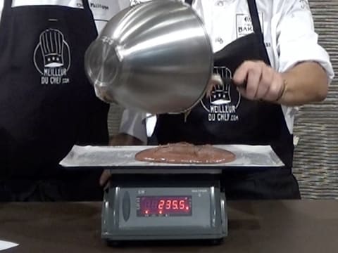 La pâte à biscuit chocolat contenu dans la cuve du batteur, est versée sur la plaque à pâtisserie graissée recouverte d'une feuille de papier sulfurisé, qui est posée sur une balance électronique qui affiche 235,5 grammes